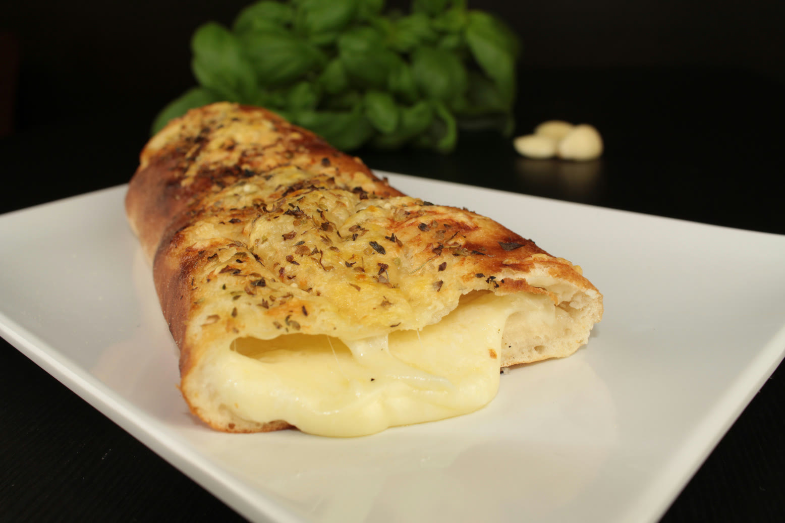 Pão de alho com queijo derretido, manjericão e alho ao fundo